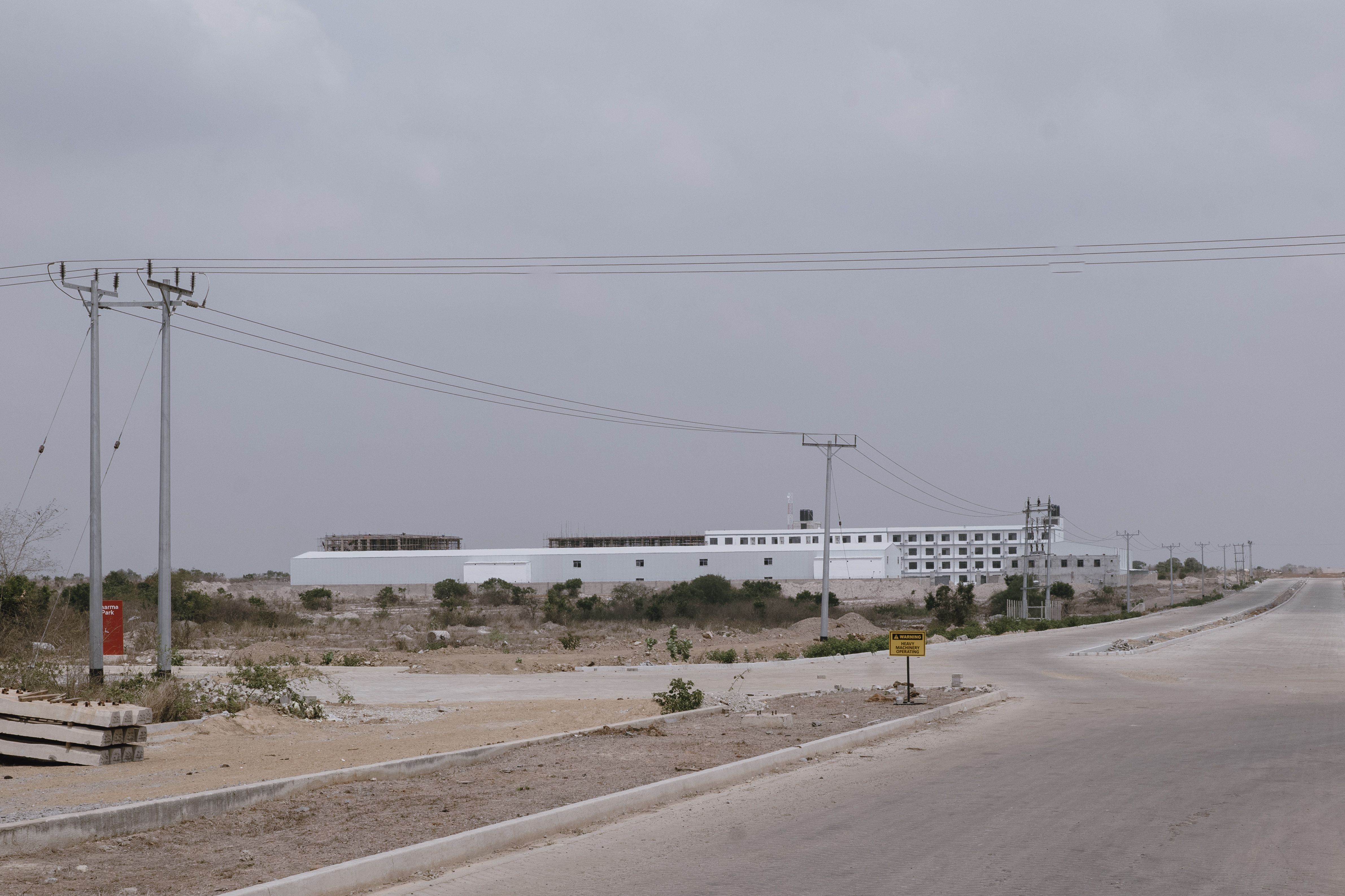 A large industrial building in a barren desert setting under an overcast sky. Power lines run along 