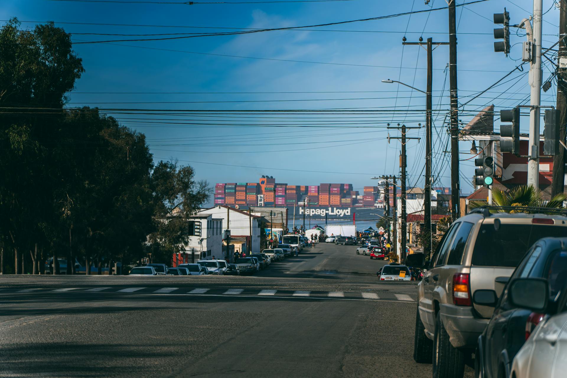 City street with vehicles parked and shipping containers visible at a harbor.
