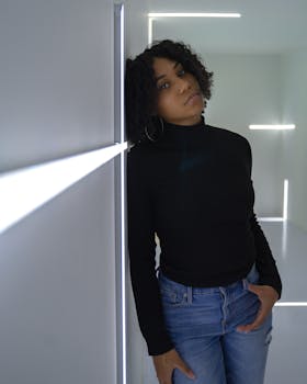 一名穿着休闲装的女子倚墙摆姿势，灯光现代简约