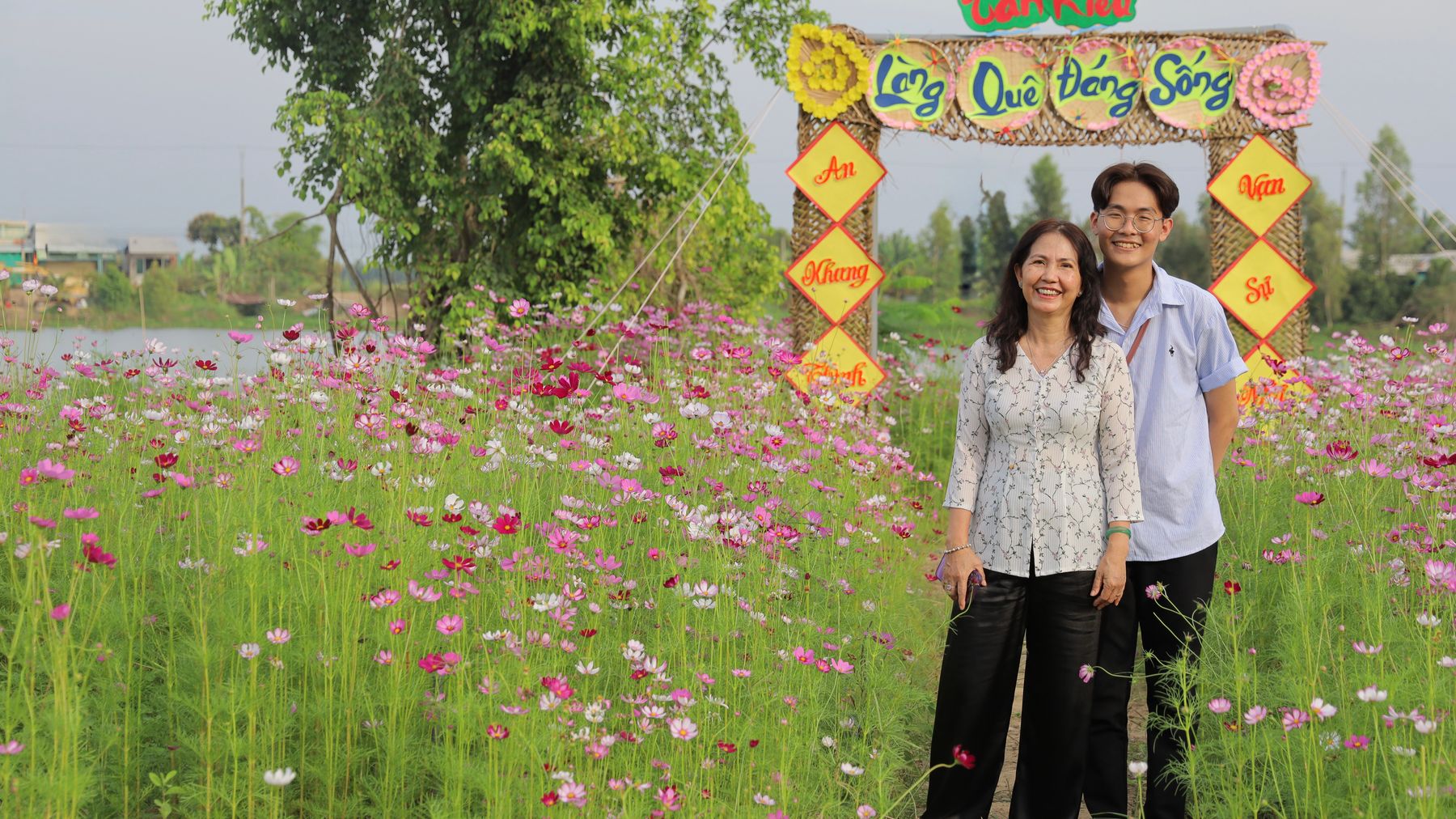Family enjoying a vibrant flower field near a colorful village gate in Tân Khâu.