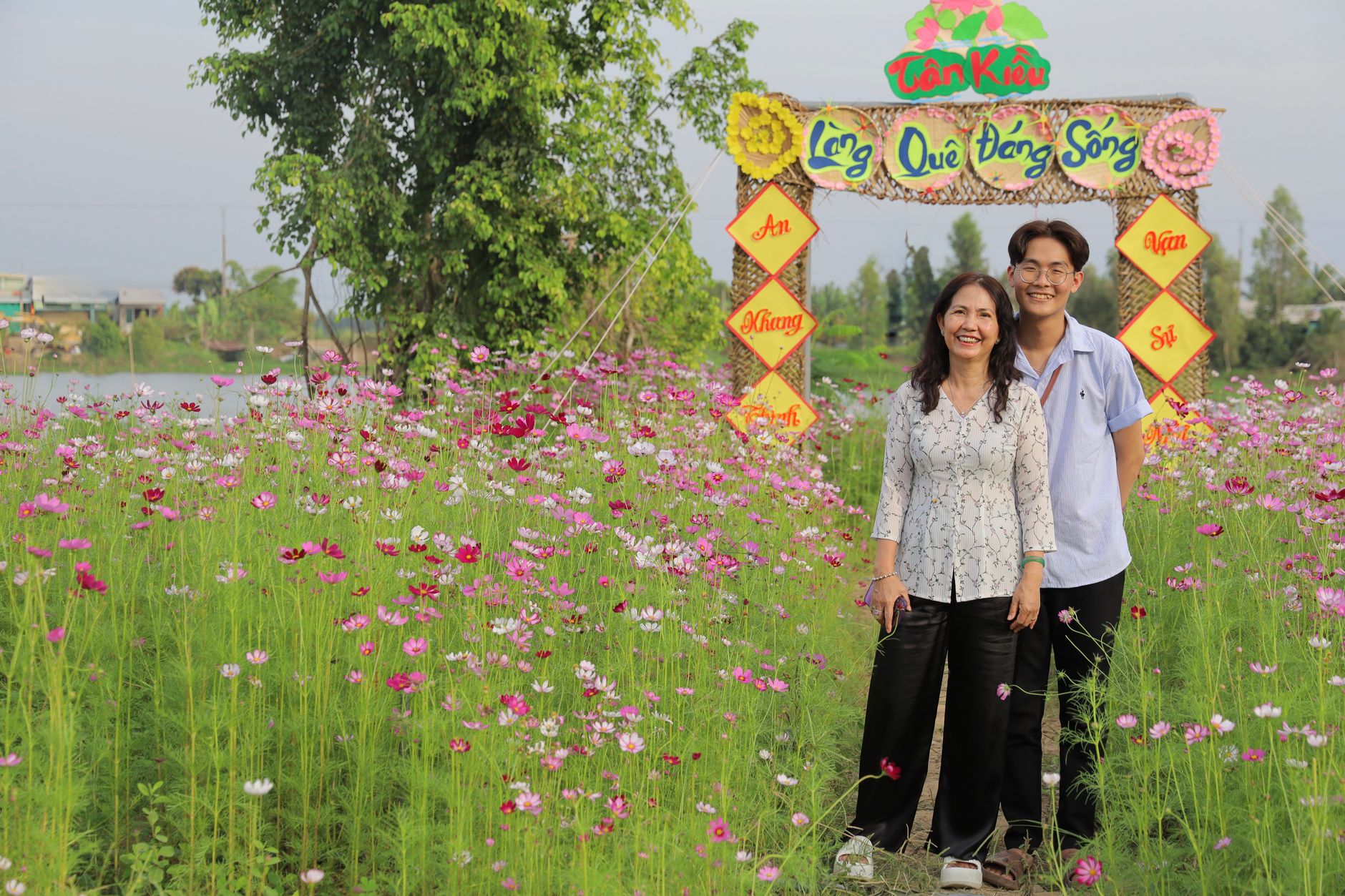 Family enjoying a vibrant flower field near a colorful village gate in Tân Khâu.