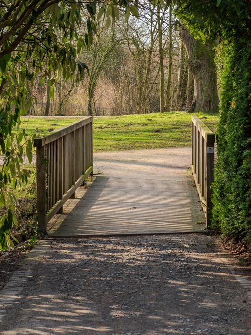 Free A peaceful walkway in a park featuring a charming wooden bridge and lush greenery. Stock Photo