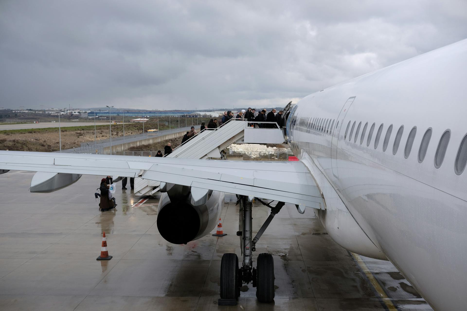 A side view of passengers boarding a large airplane at an airport on an overcast day.
