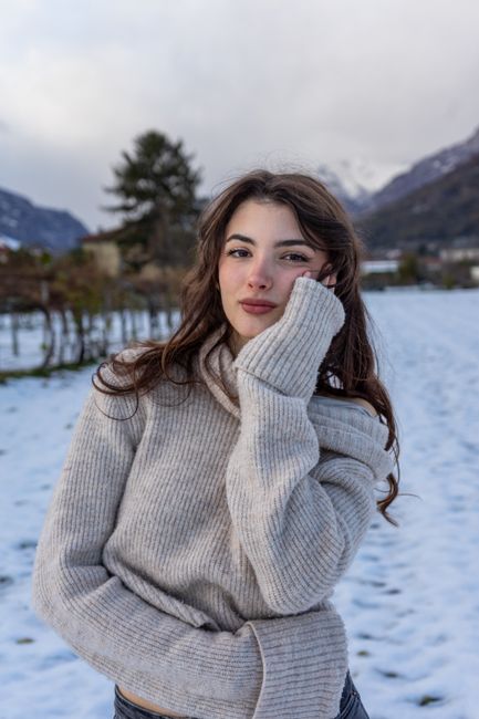 A young woman poses in a winter scene with mountains in Italy.