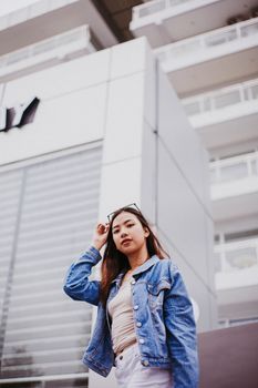 一位自信的年轻女性穿着休闲牛仔夹克，在现代建筑前摆姿势