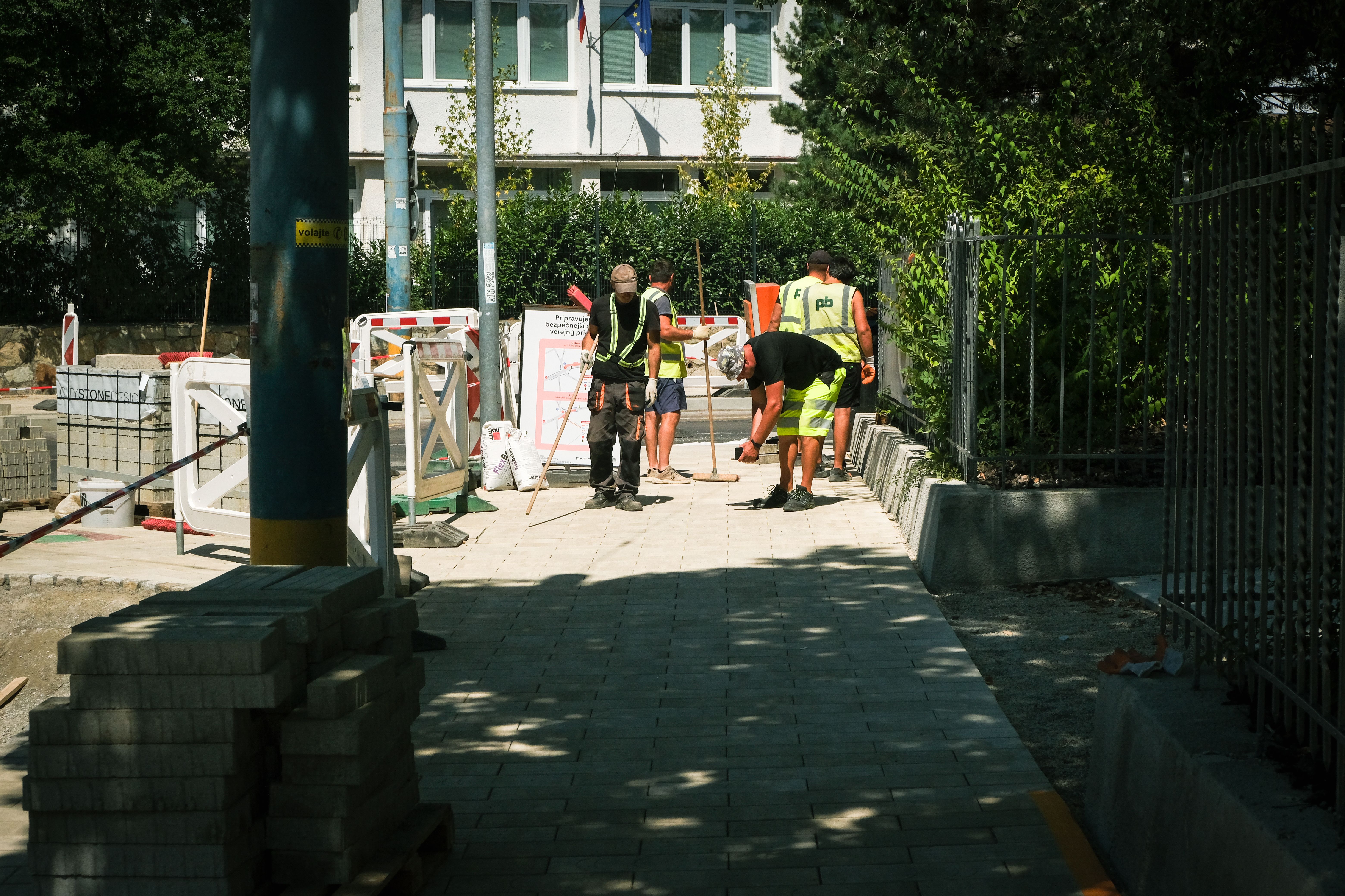 Als privater Bauherr ausschreiben: geht das? – Team of construction workers paving a sidewalk outdoors on a sunny day in Bratislava.