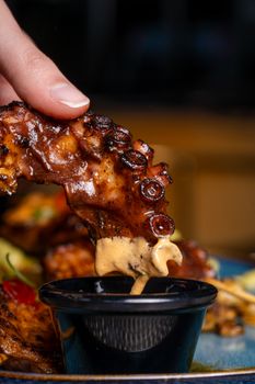 Close-up of a grilled octopus tentacle being dipped in sauce, showcasing its rich texture and flavor.