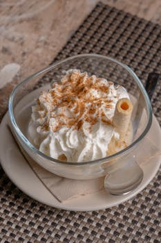 A tempting dessert in a glass bowl topped with whipped cream and cinnamon, accented with wafer roll.