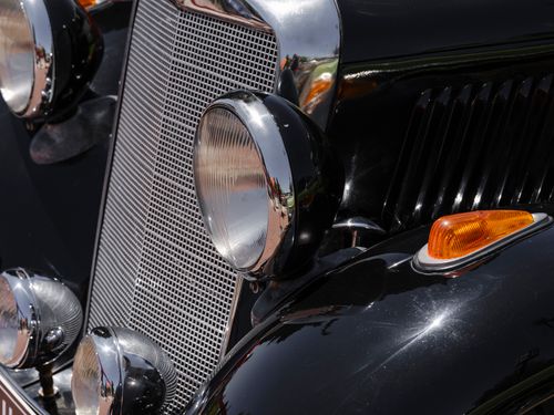 Free Detailed view of a chrome-accented vintage car headlight and grill, reflecting its classic elegance. Stock Photo