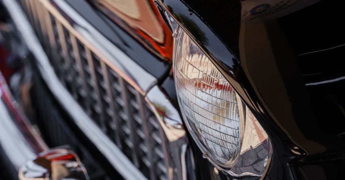 Detailed close-up of a vintage car's shiny headlight and grille, reflecting its classic design.