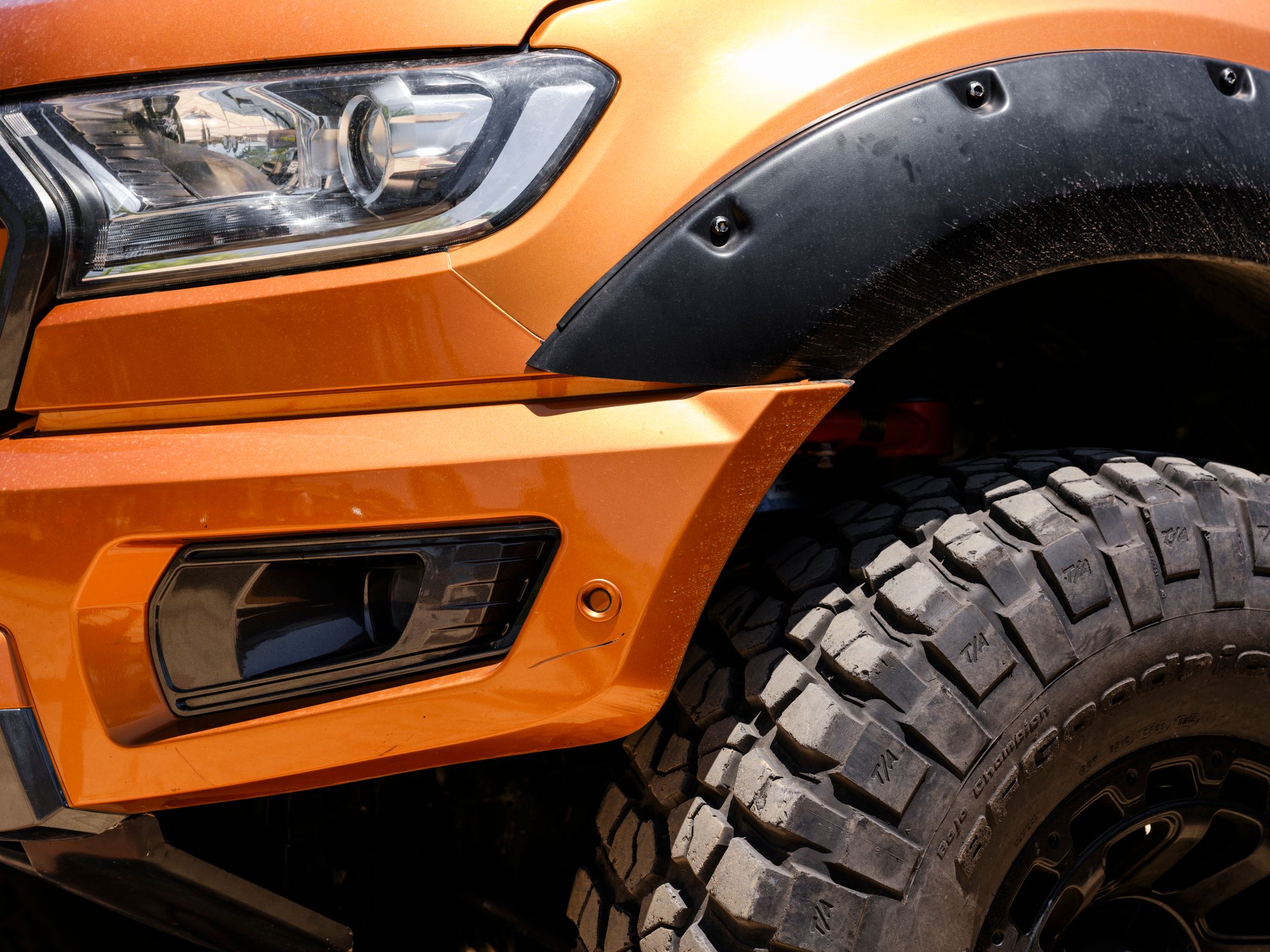 Close-up of a black plastic fender flare and wheel arch trim on an orange off-road pickup truck
