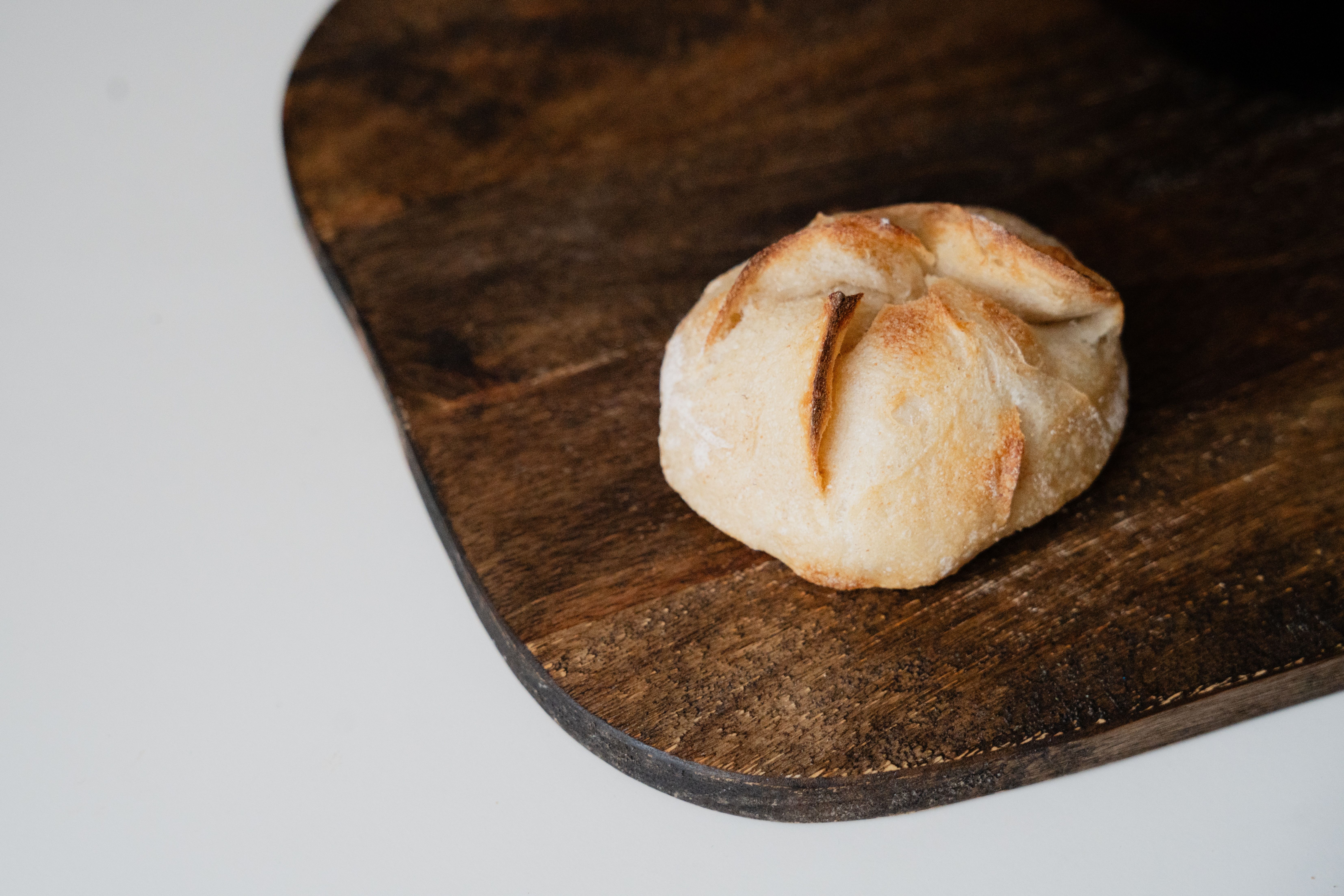A freshly baked rustic bread roll placed on a wooden cutting board. Perfect for bakery promotions.