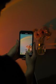 A person captures a bouquet of flowers using a smartphone in dim lighting.