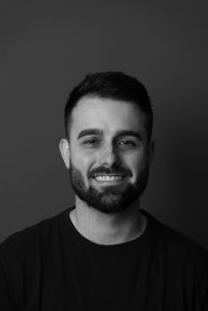 Black and white professional headshot portrait of a smiling adult male against plain background.