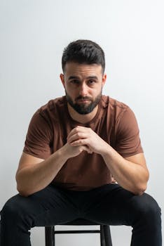 Portrait of a confident adult man sitting with hands clasped in a minimalist setting
