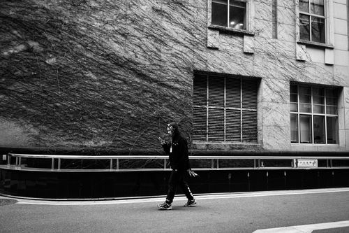 Free Monochrome image of a person walking along an urban street, capturing city life. Stock Photo