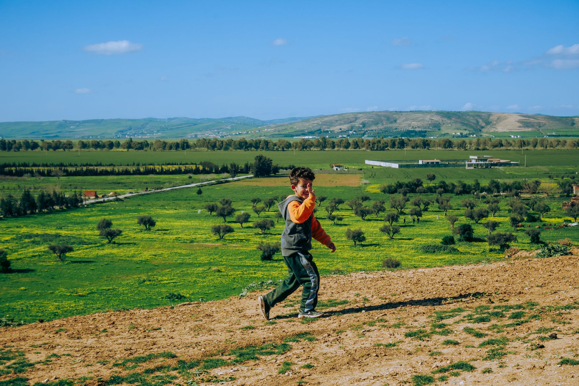 A child joyfully runs on a hillside overlooking green fields in Sidi Thabet, Tunisia.