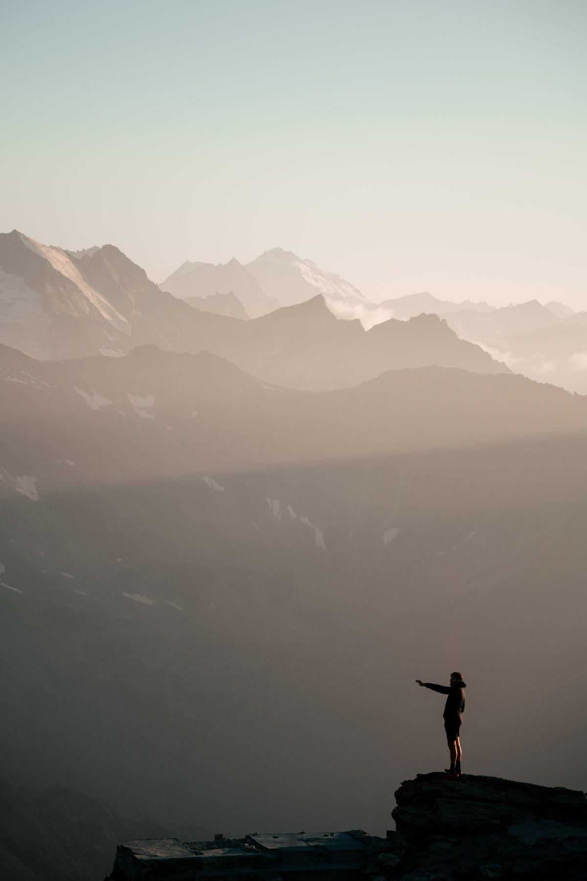 Person standing on a mountain summit at sunrise, pointing toward the view, symbolizing the gap between goal-setting and actual achievement