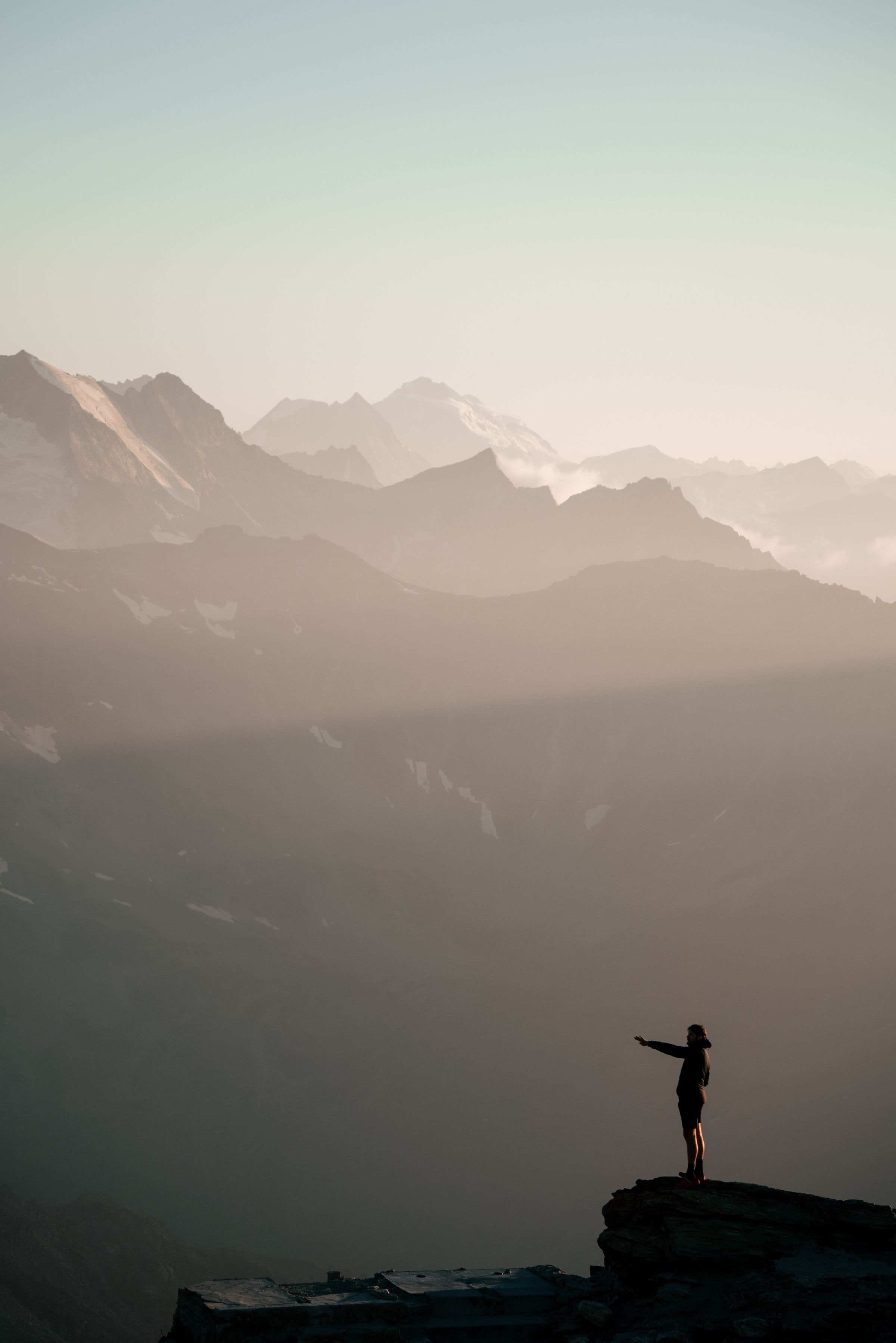 A person standing on a mountain summit at sunrise, looking out over hazy peaks