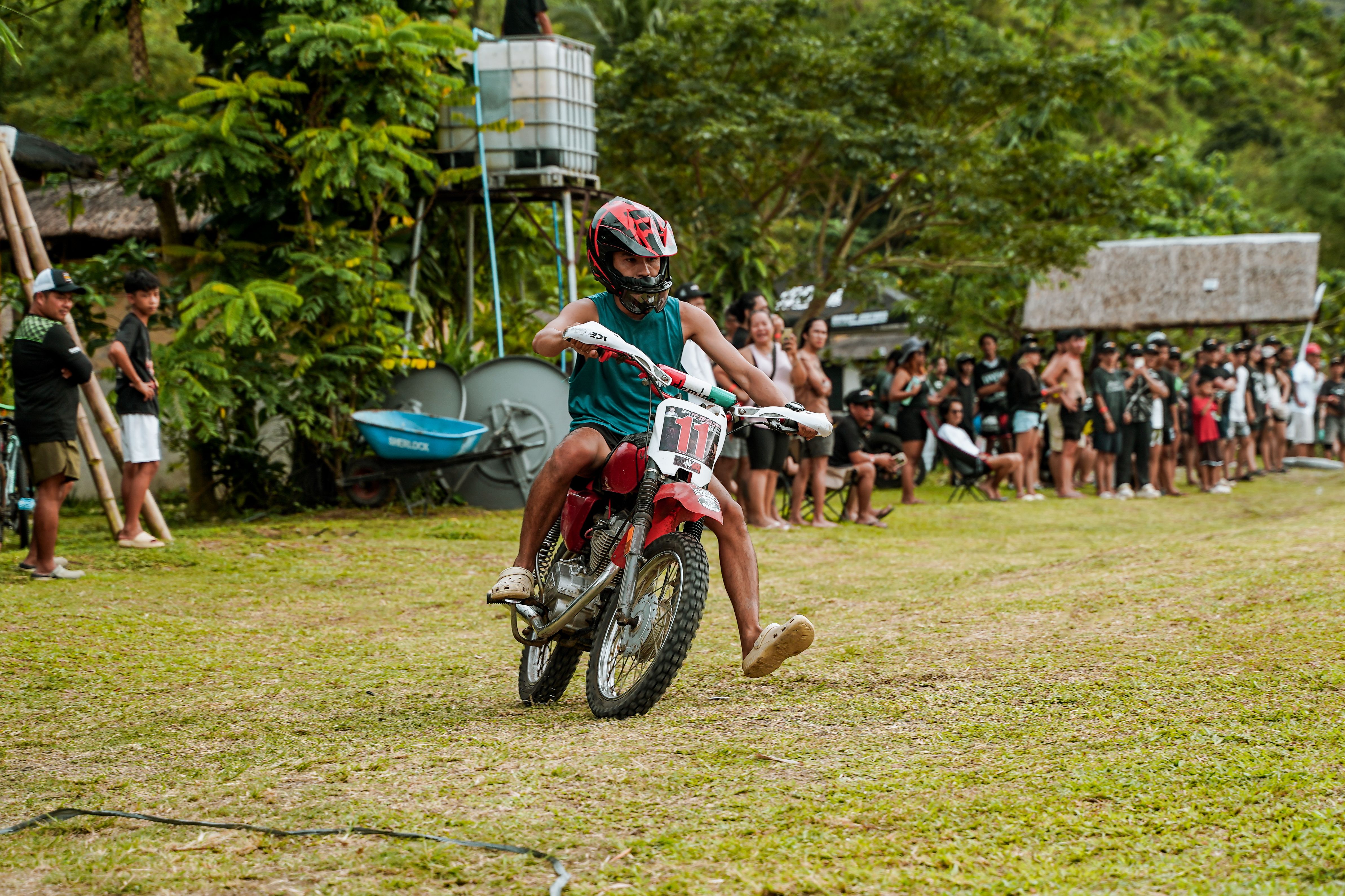 A crowded rural Philippine cockfighting arena, handlers holding roosters, spectators watching under muted afternoon light