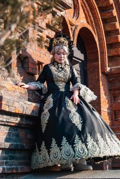 Woman in ornate traditional gown with red brick architectural background.