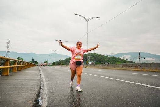 Un corridore trionfante festeggia durante una maratona su una strada cittadina con montagne sullo sfondo.