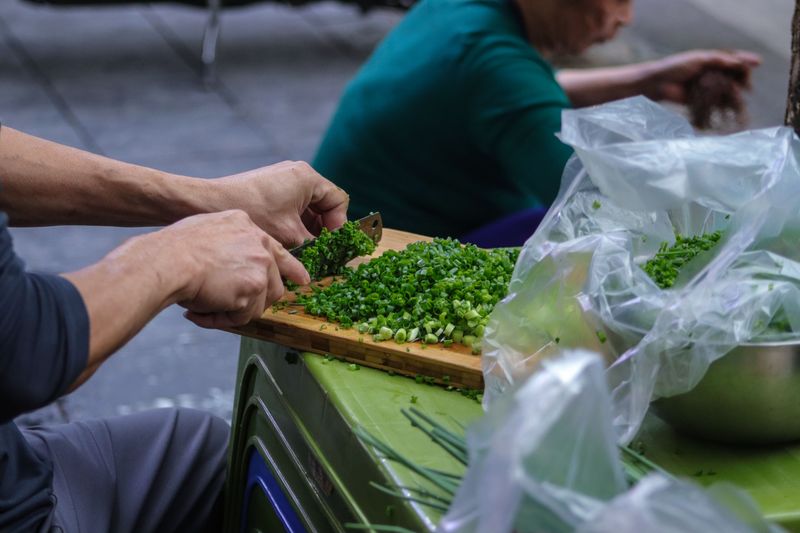 Close-up of hands chopping spring onions on a board, showcasing fresh ingredients.