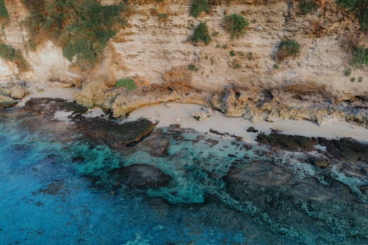 A breathtaking aerial view of a serene beach in Bali, showcasing clear waters and rocky cliffs.