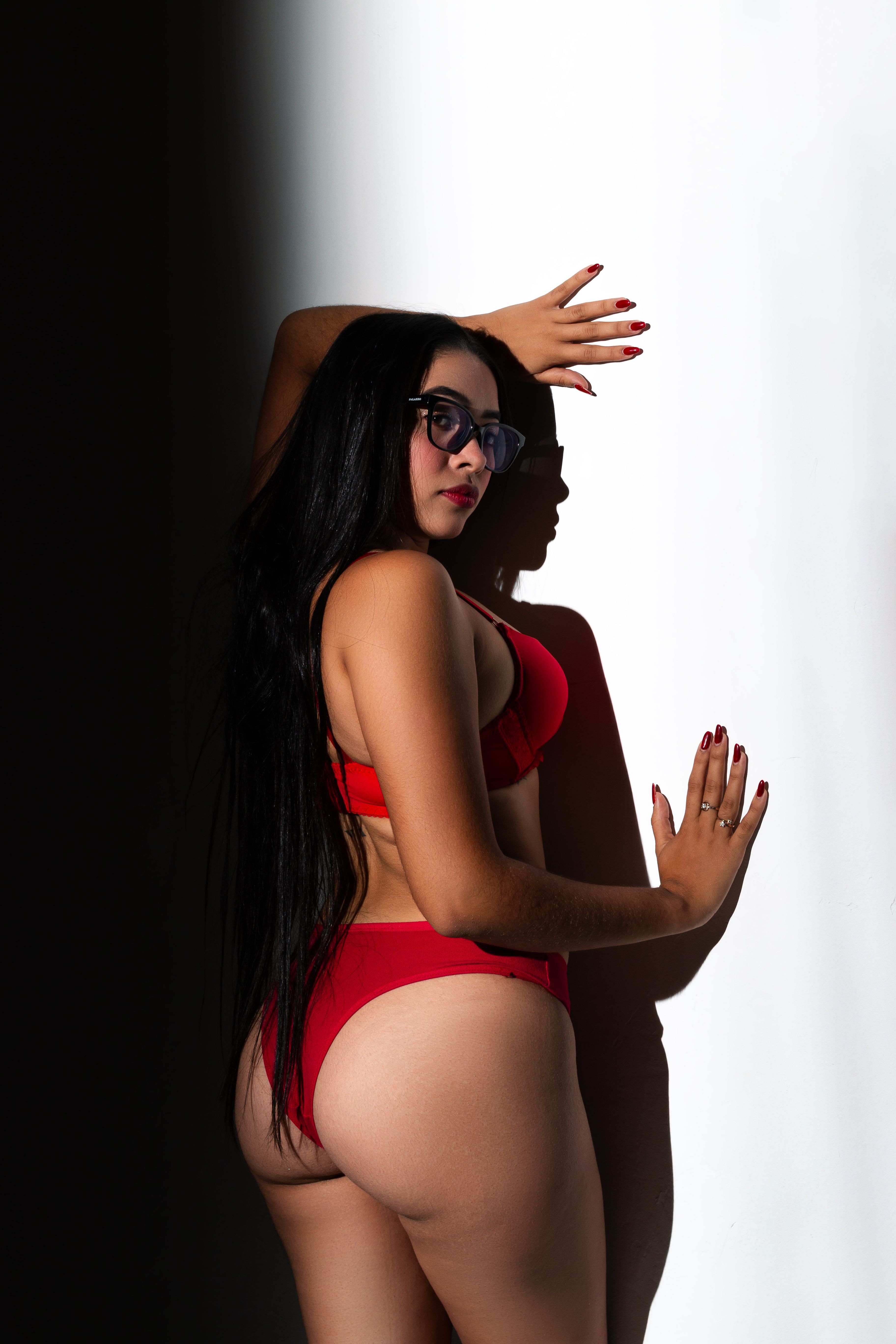 Confident woman wearing a red bikini poses against a sharp shadow contrast backdrop.