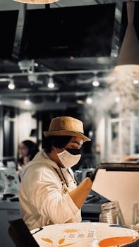 Barista in hat and mask makes coffee in a stylish, modern cafe.