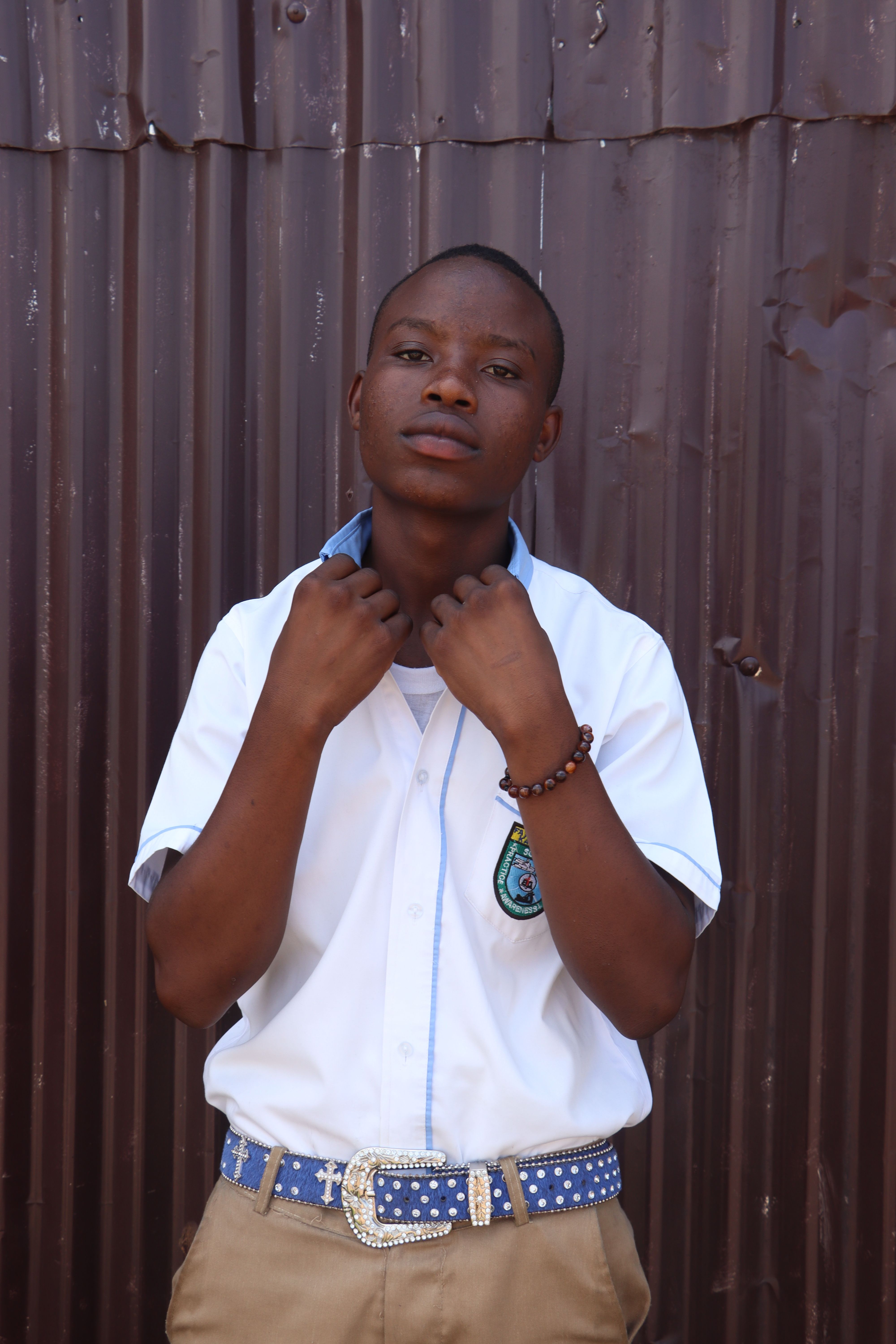 Confident young man in white uniform and blue belt standing against a metal wall.