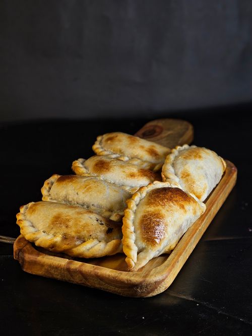 Free Delicious golden-brown empanadas placed on a wooden board perfect for a tasty snack. Stock Photo