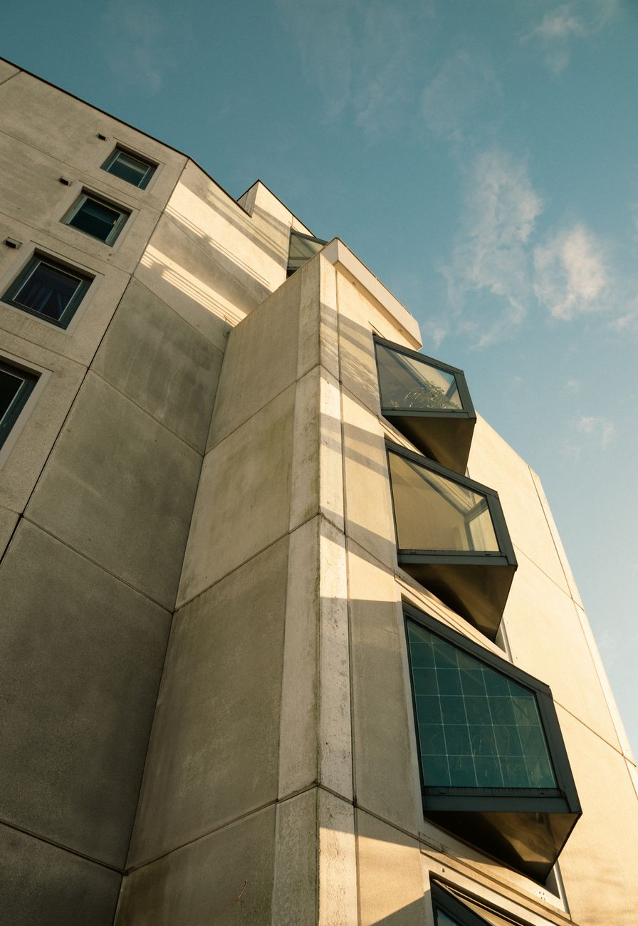 A low-angle view of a modern concrete building with large windows against a clear sky.