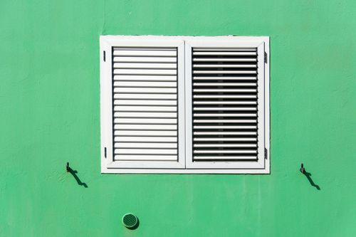 Free Bright green wall with white louvered shutters casting shadows in daylight. Stock Photo