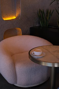 A stylish cafe interior with soft lighting, a plush chair, and a cup of coffee on a marble table.