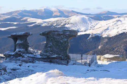 Free Snow-capped Babele rock formations stand against the backdrop of the Bucegi Mountains in Romania. Stock Photo