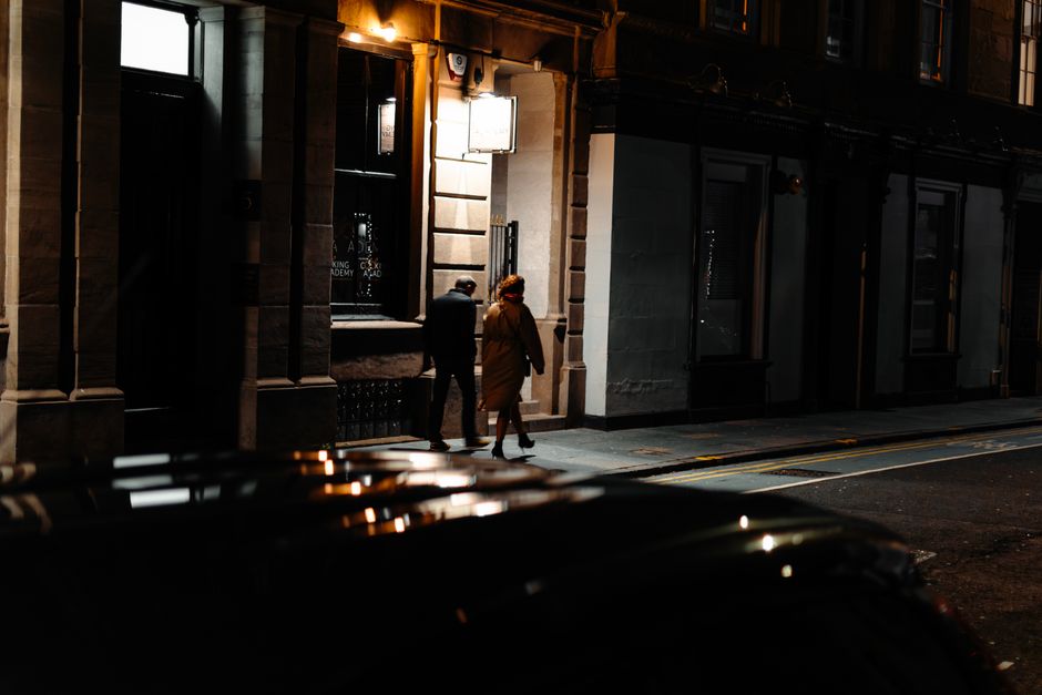 Candid night scene of two adults walking on a street in Edinburgh, Scotland.