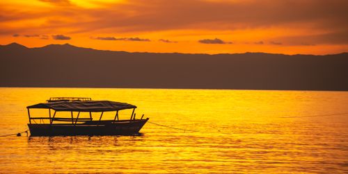 Free A tranquil boat silhouetted against a stunning orange Zanzibar sunset. Stock Photo