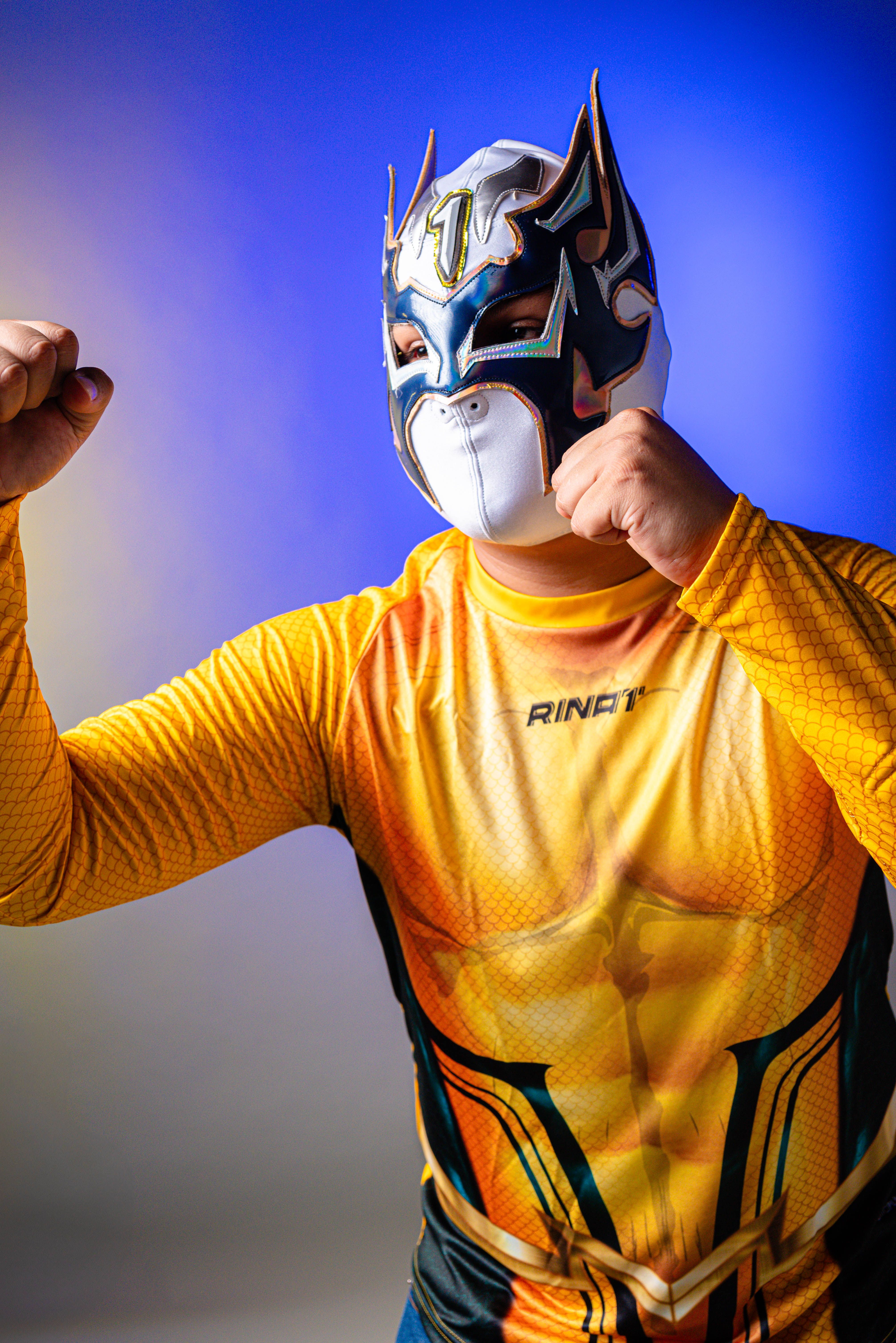 Mexican luchador wearing a vibrant mask and costume, striking a dynamic pose against a colorful background.