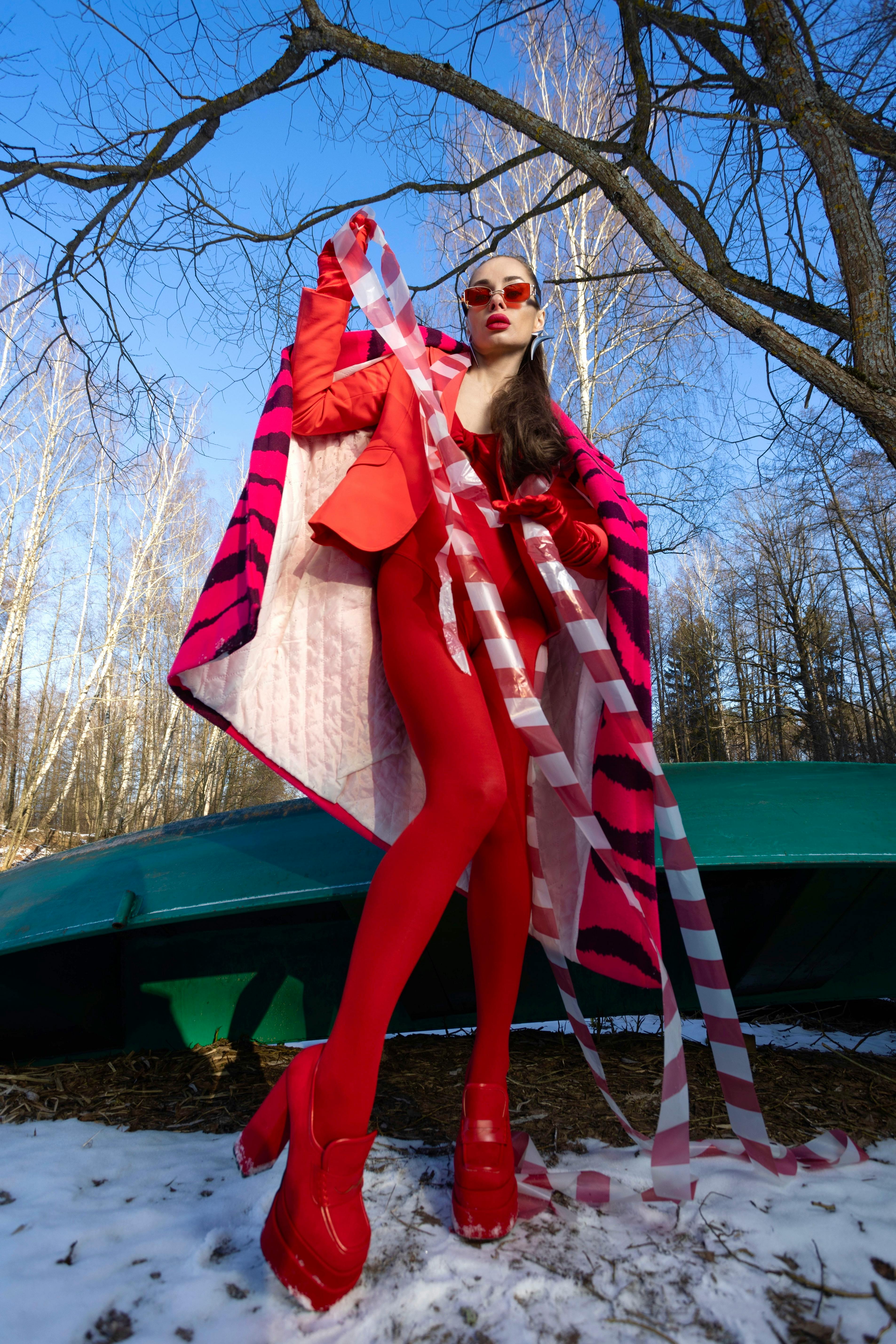 Stylish model in bold red outfit posing outdoors with colorful fabric.