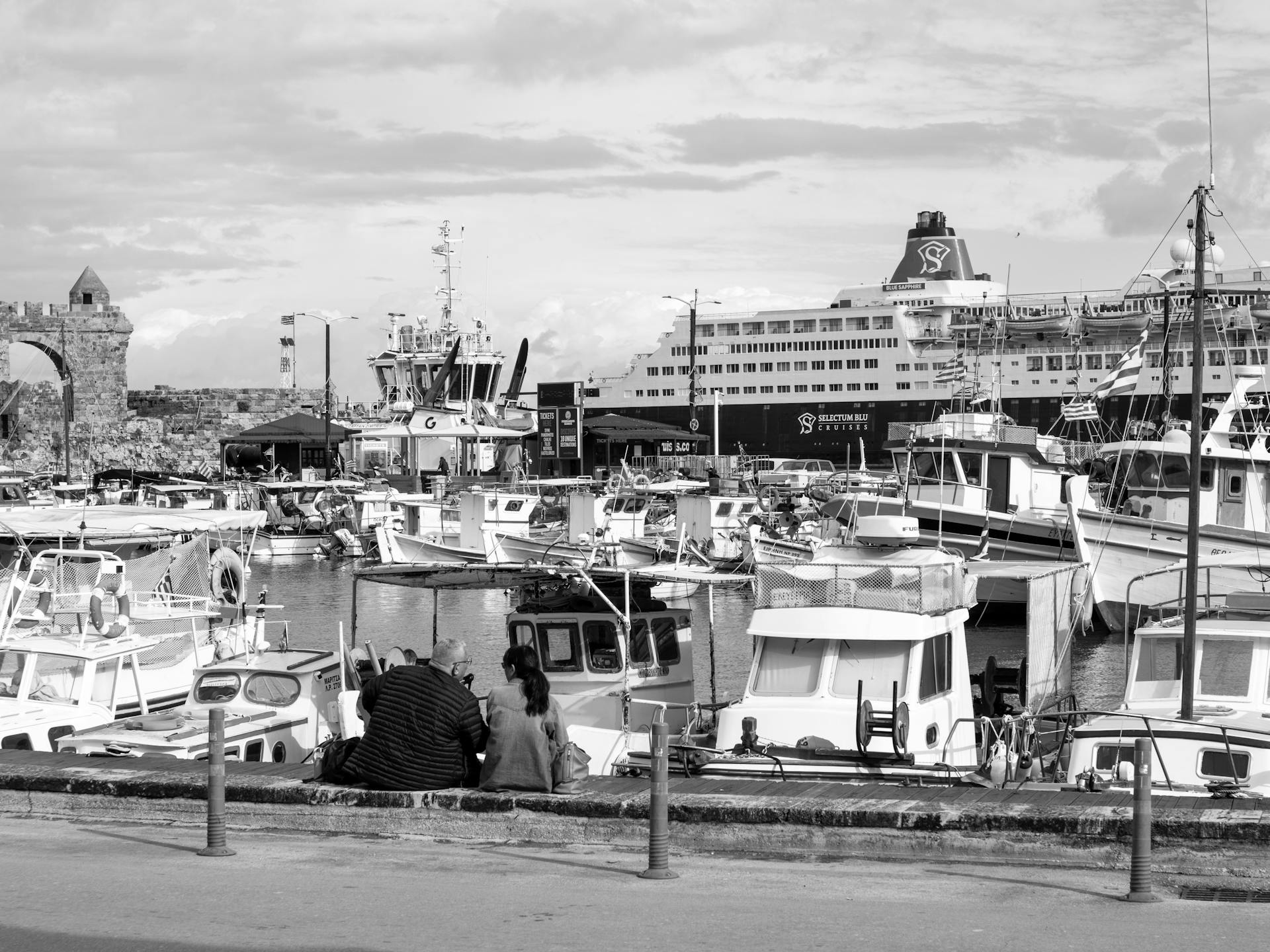 Black and white photo of a busy harbor with boats, cruise ship, and historical architecture.