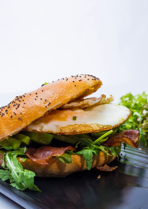 Free Tasty bagel sandwich with egg, bacon, and greens on a plate, perfect breakfast choice. Stock Photo