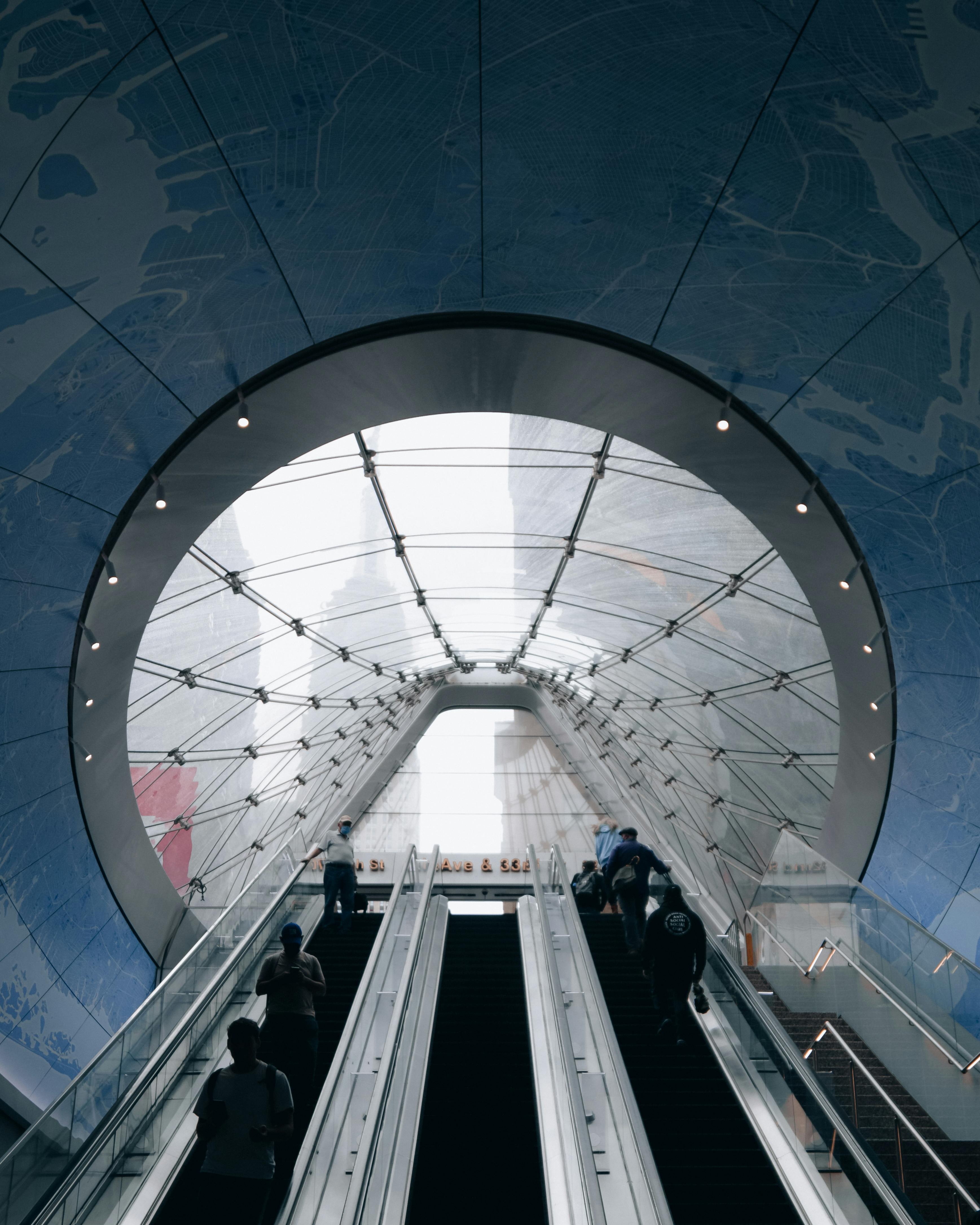 People using an escalator at a modern subway entrance in New York City.