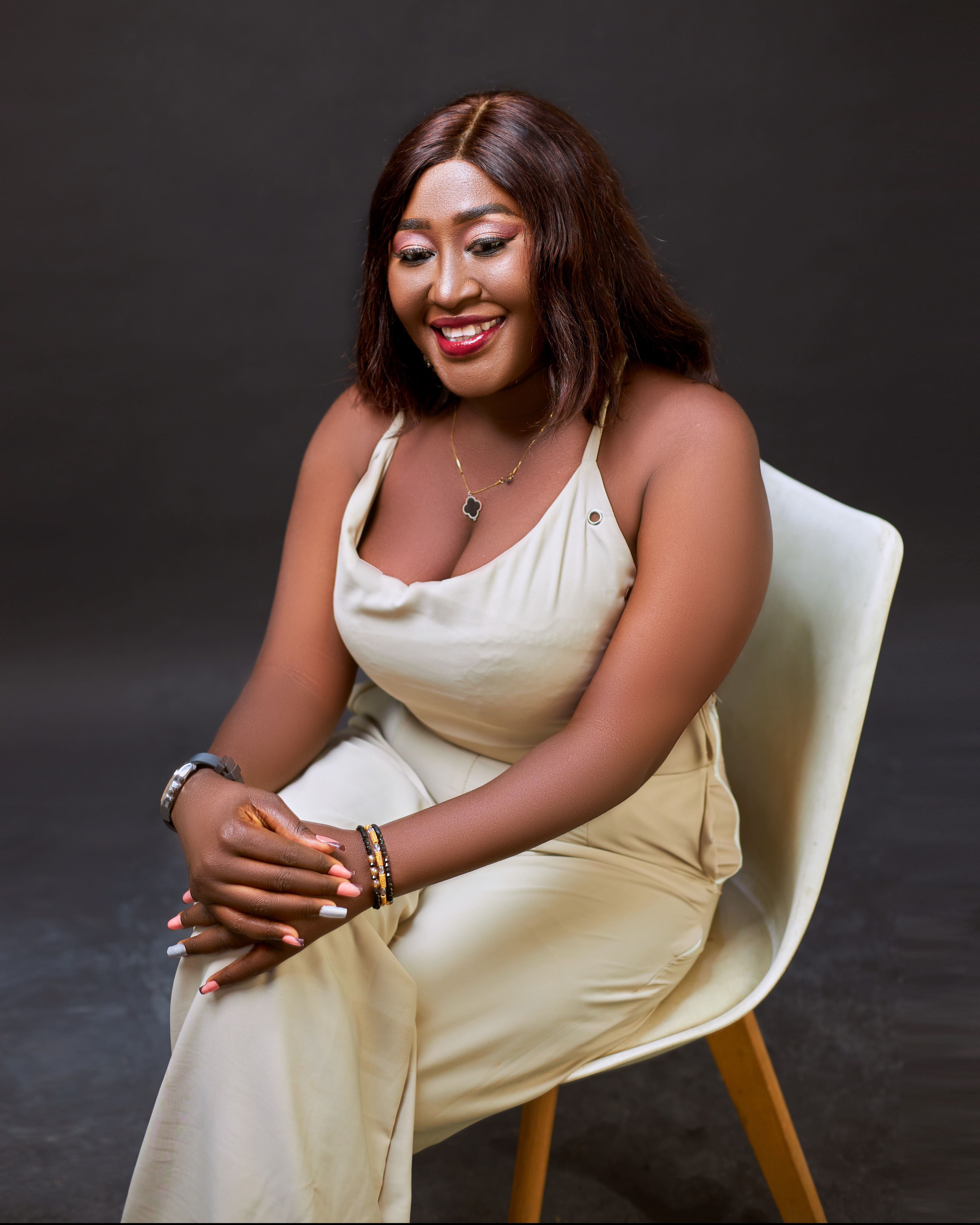 Confident woman seated on chair smiling warmly against dark background.