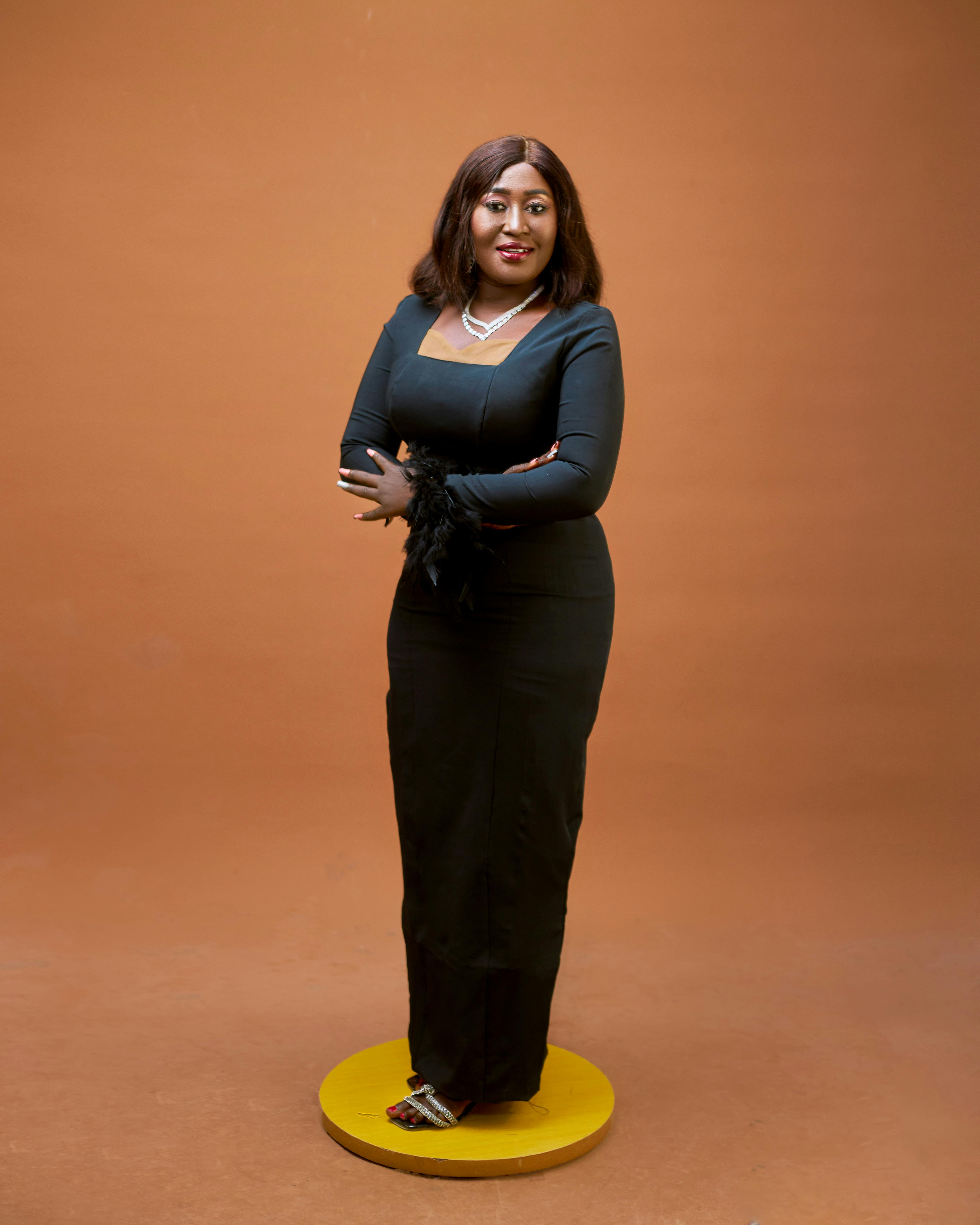 Stylish portrait of a woman in a black evening gown with an orange backdrop, exuding elegance.