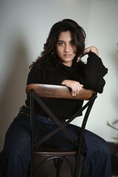 Portrait of a confident woman seated on a chair indoors.