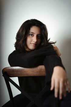 Artistic portrait of a woman in a black sweater leaning on a chair.