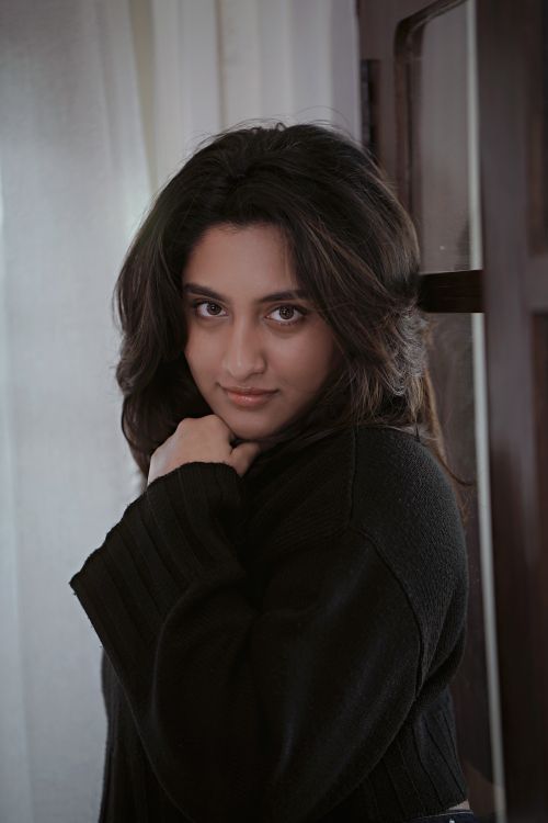 Free Portrait of a young woman in a cozy, dark sweater indoors. Stock Photo
