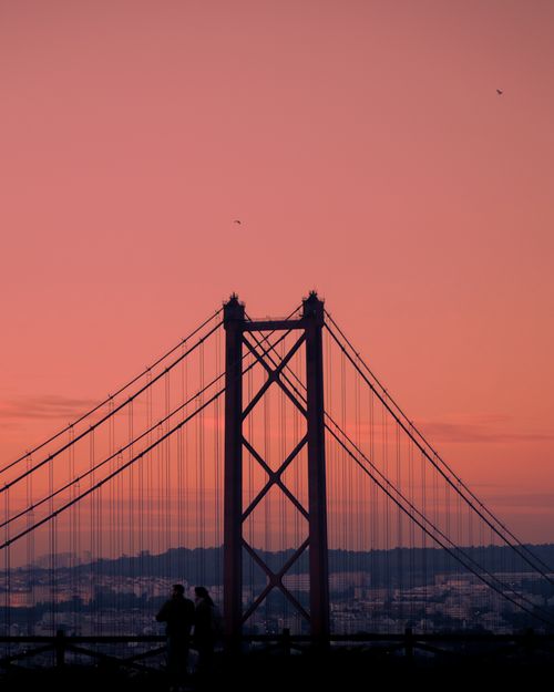 Free Silhouette of Lisbon's 25 de Abril Bridge at sunset with people in foreground. Stock Photo