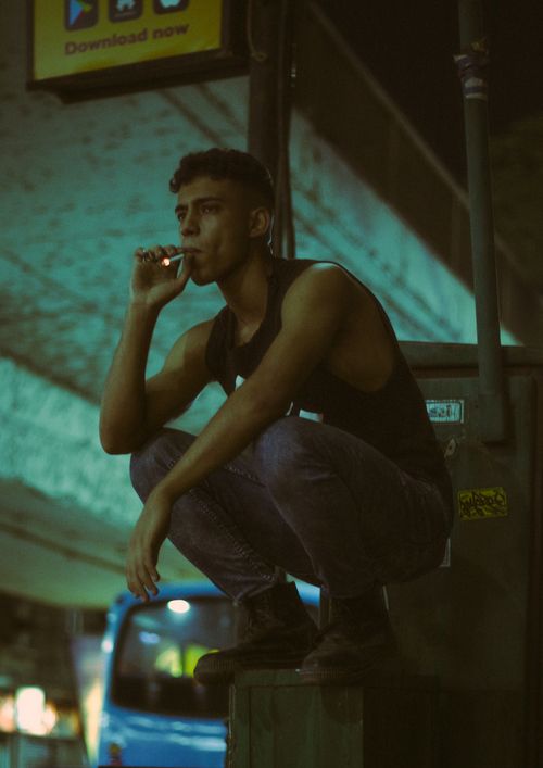 Free A young man smokes while squatting in an urban setting at night in Egypt. Stock Photo